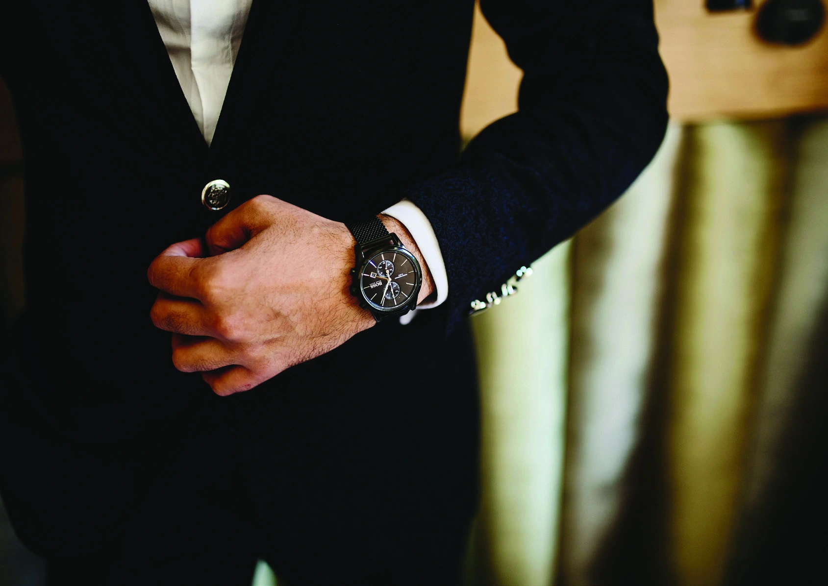 The finishing details of a dark tailored jacket and watch